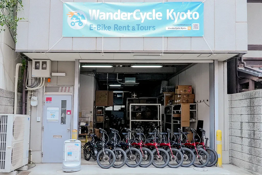 WanderCycle Kyotoの店頭の写真。水色の布看板が建物についており、レンタル用のe-Bikeが並んでいる。