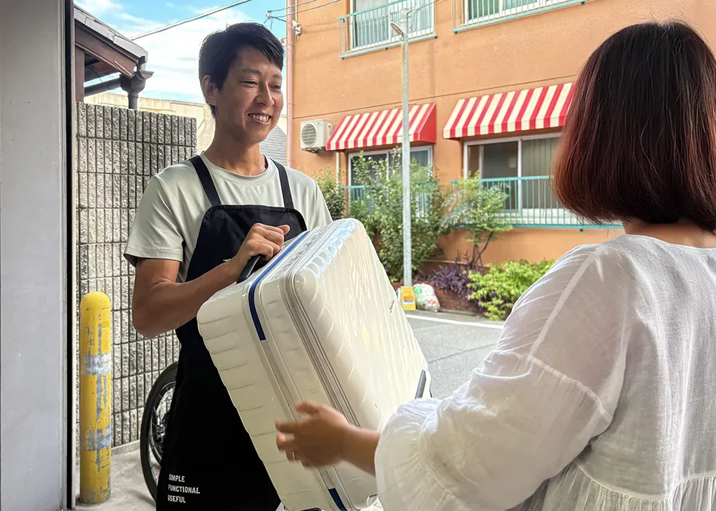 「荷物」預かりオプションを利用するために、店舗スタッフに持参したキャリーケースを預けている様子。